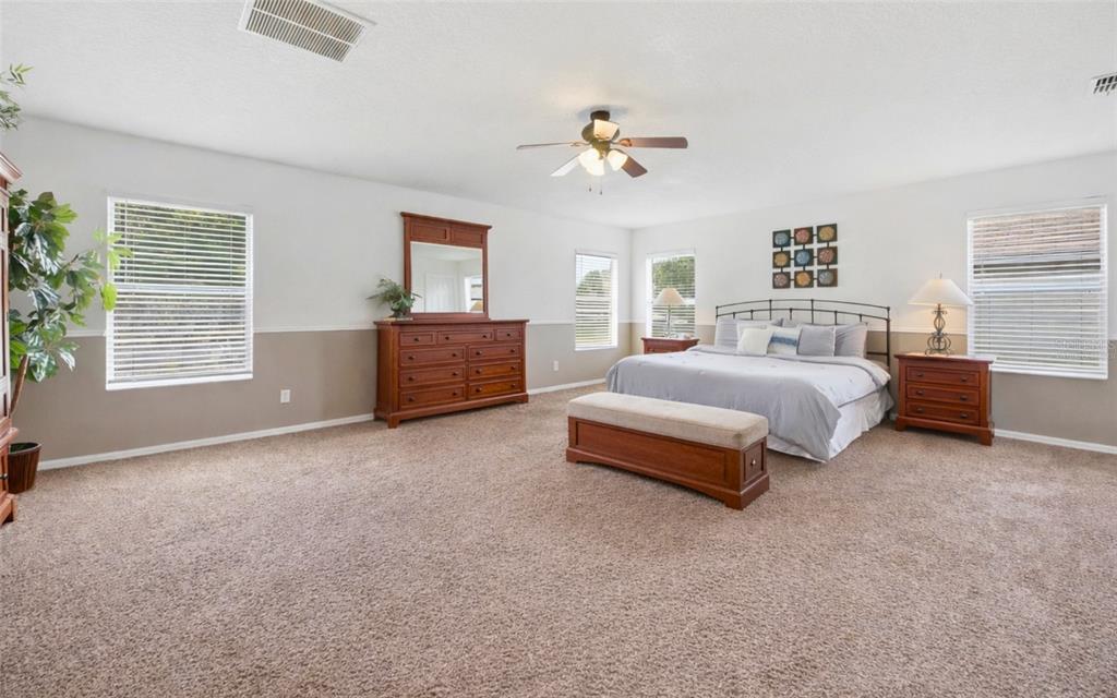 A spacious bedroom features beige carpet, two-toned walls, a wooden dresser, and a king-sized bed — 111 ALDRIDGE LANE, DAVENPORT, FL
