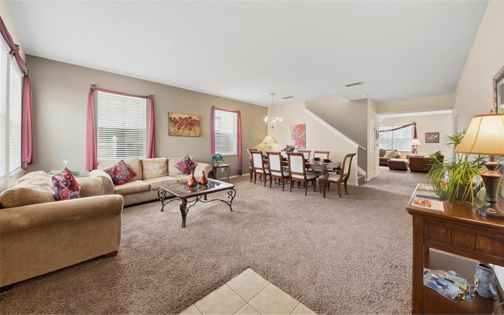 A living and dining area with beige walls, brown carpet, and a wooden dining set — 111 ALDRIDGE LANE, DAVENPORT, FL