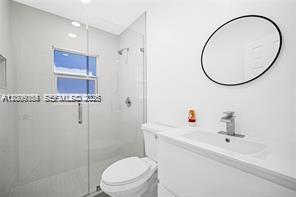 A modern bathroom features a glass-enclosed shower, a white vanity, and a round wall mirror — 1301 Sharar Ave, Opa-Locka FL 33054, OPA-LOCKA, FL