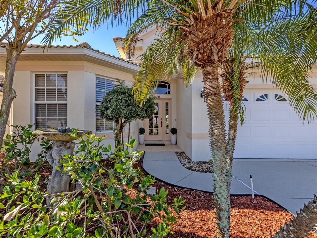A single-story house exterior features a palm tree, a stone fountain, and a paved walkway — 404 PINEWOOD LAKE DRIVE, VENICE, FL