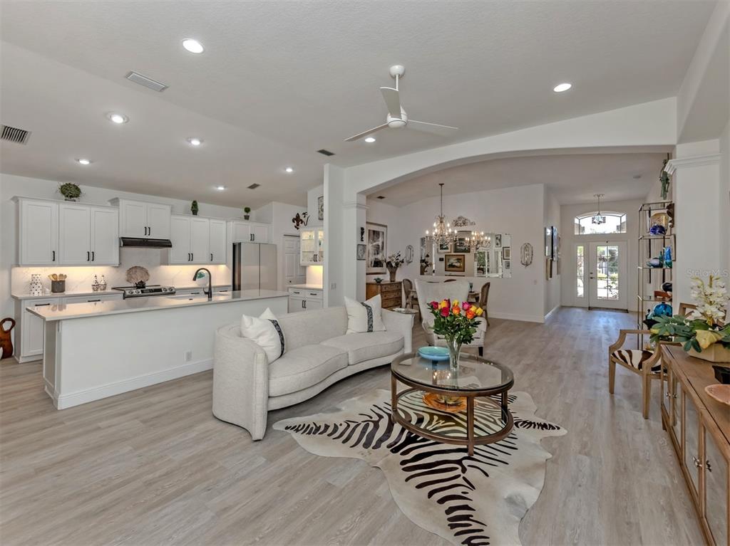 A bright open-concept kitchen and living area with white cabinetry, light flooring, and zebra rug — 404 PINEWOOD LAKE DRIVE, VENICE, FL