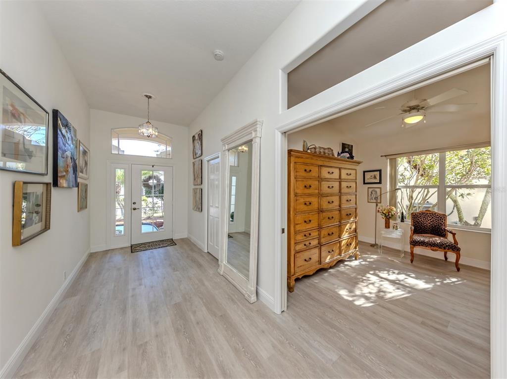 A bright entryway with light wood flooring leads to a room featuring a large dresser — 404 PINEWOOD LAKE DRIVE, VENICE, FL