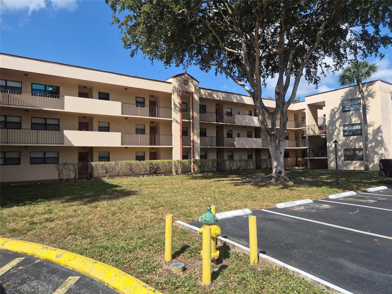 A three-story apartment building with beige stucco walls and a large tree in front — 3252 Foxcroft Road # 113, Miramar FL 33025, MIRAMAR, FL