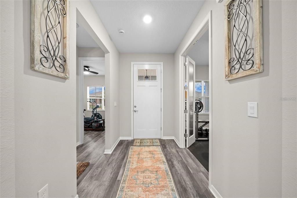 A foyer with gray wood-look flooring, a white front door, and two adjacent rooms — 10564 SW 98TH LANE, OCALA, FL