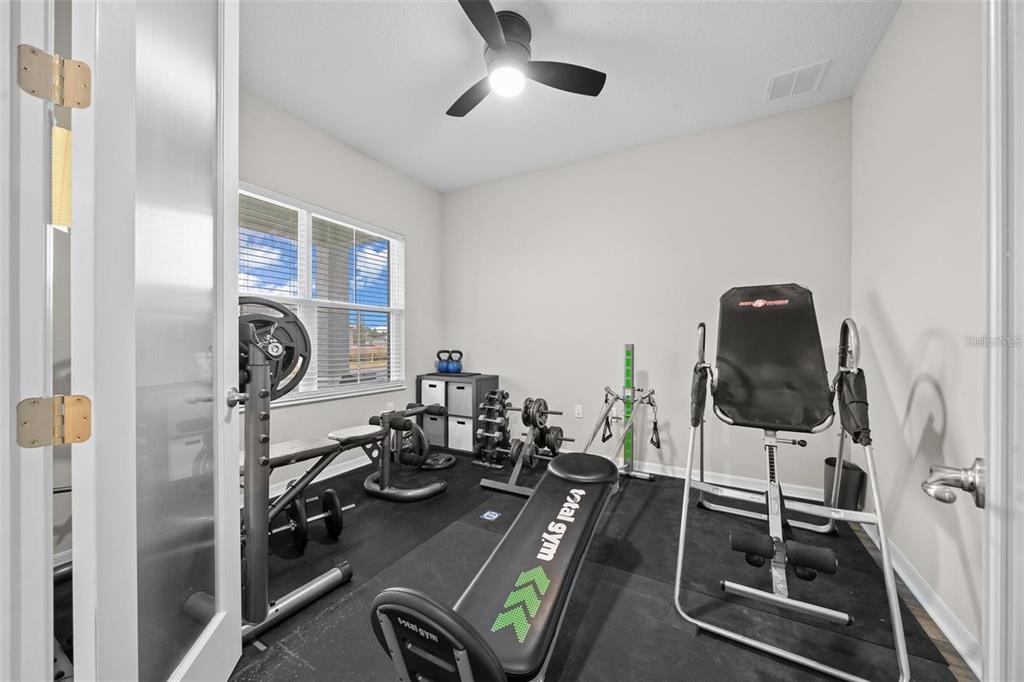 A home gym features a Total Gym machine, an inversion table, and weights on rubber flooring — 10564 SW 98TH LANE, OCALA, FL