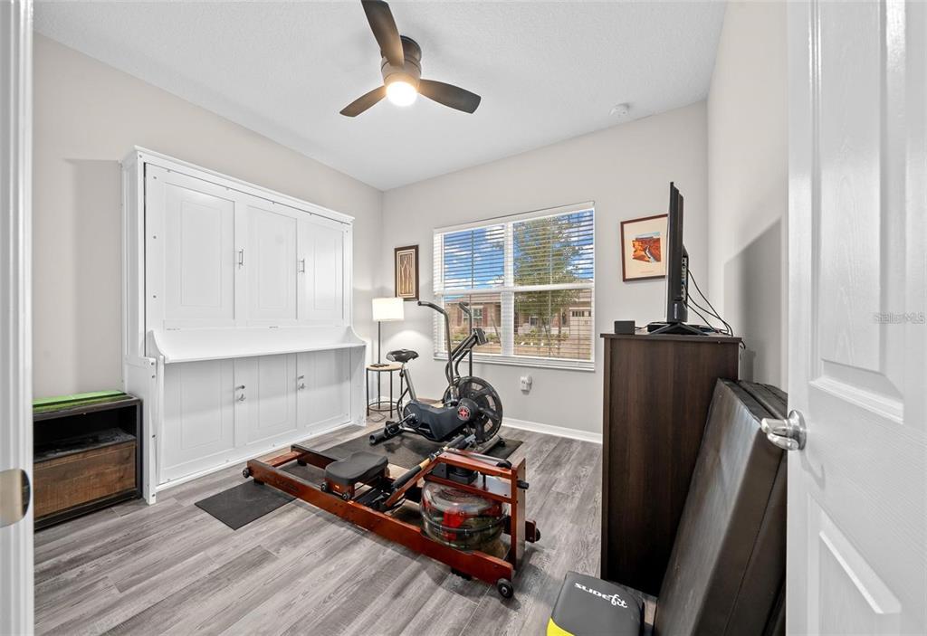 A home gym features a rowing machine, exercise bike, Murphy bed, and wood-look flooring — 10564 SW 98TH LANE, OCALA, FL