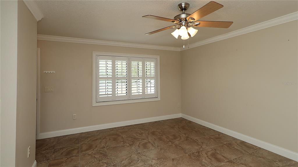 An empty room features beige walls, tile flooring, a ceiling fan, and plantation shutters — 1915 SW 34TH COURT, OCALA, FL