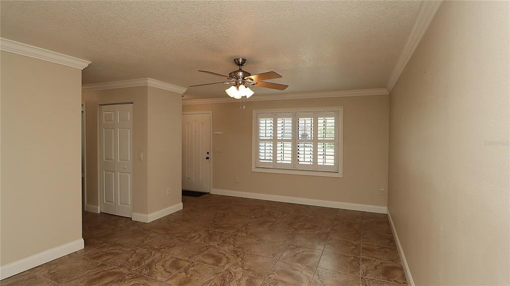 A living room with beige walls, tile flooring, a ceiling fan, and plantation shutters — 1915 SW 34TH COURT, OCALA, FL