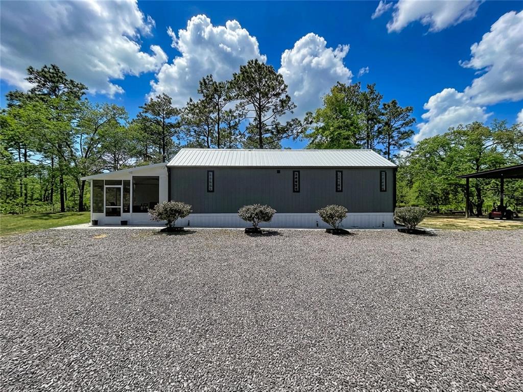A gray metal-sided building with a white roof and a screened porch sits on gravel — 10388 S SUNCOAST BOULEVARD, HOMOSASSA, FL