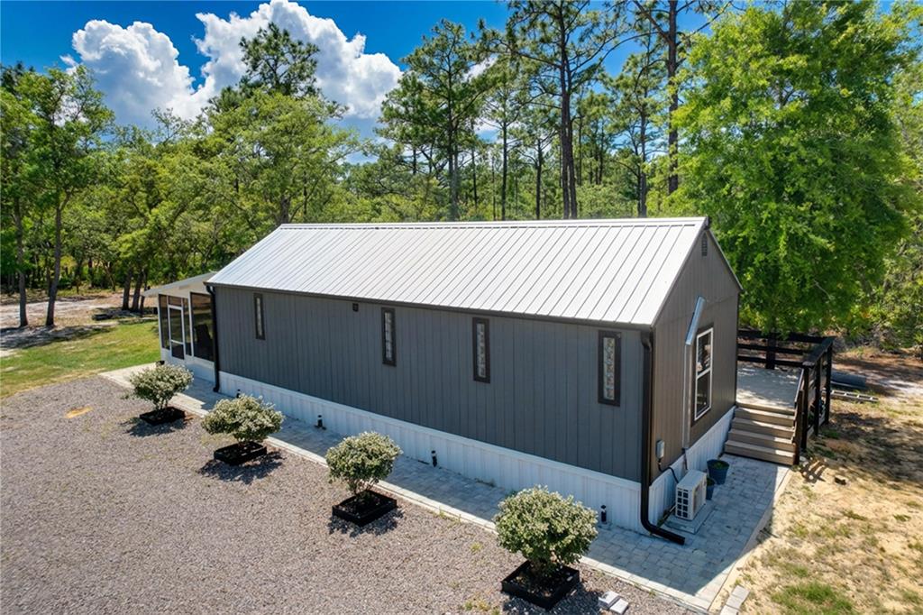 An exterior view of a modern, dark-sided manufactured home with a metal roof and landscaping — 10388 S SUNCOAST BOULEVARD, HOMOSASSA, FL