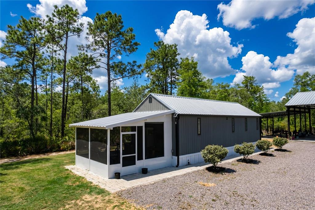 A gray metal-sided house with a screened-in porch sits on a gravel lot near trees — 10388 S SUNCOAST BOULEVARD, HOMOSASSA, FL
