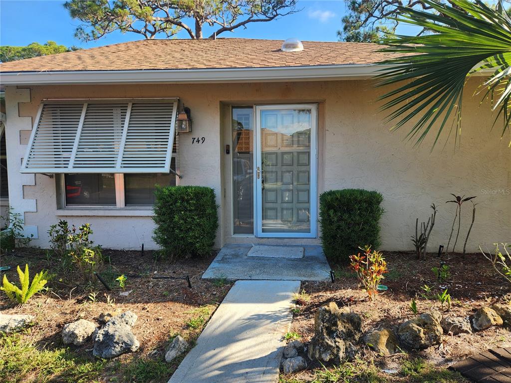 The exterior of a single-story house features a front door, a window with shutters, and landscaping — 749 N JEFFERSON AVENUE UNIT 749, SARASOTA, FL