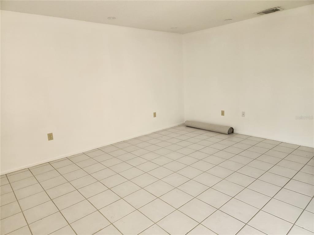 An empty room features white walls, a tiled floor, and a rolled-up piece of carpet — 749 N JEFFERSON AVENUE UNIT 749, SARASOTA, FL