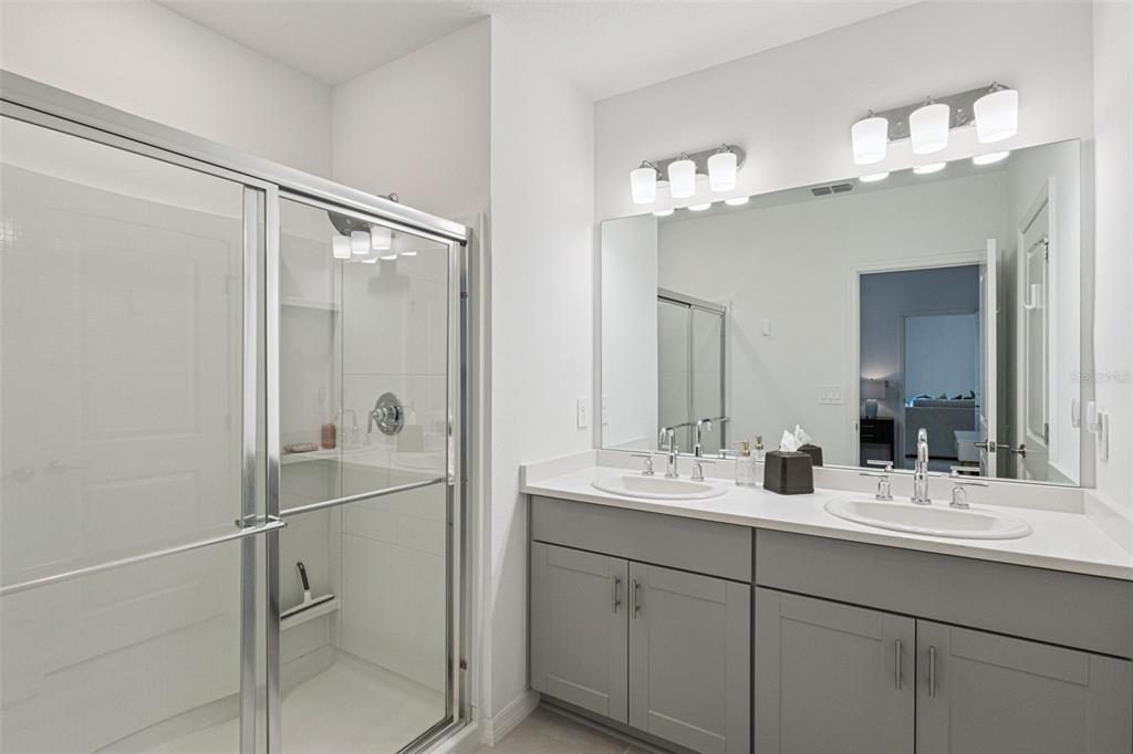 A bathroom features a glass-enclosed shower, a double vanity with gray cabinets, and a mirror — 1099 CALICO POINTE CIRCLE, GROVELAND, FL
