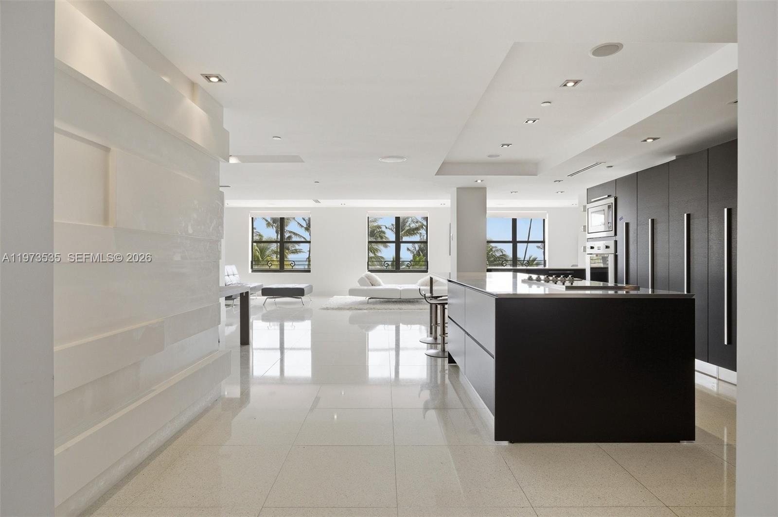 A modern kitchen with a black island and cabinetry overlooks a bright, minimalist living area — 1330 Ocean Dr, Miami Beach FL 33139, MIAMI BEACH, FL