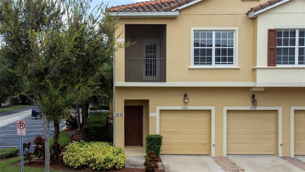 A two-story townhouse exterior features a brown front door, a balcony, and two garage doors — 7531 PELLHAM WAY UNIT 77, KISSIMMEE, FL