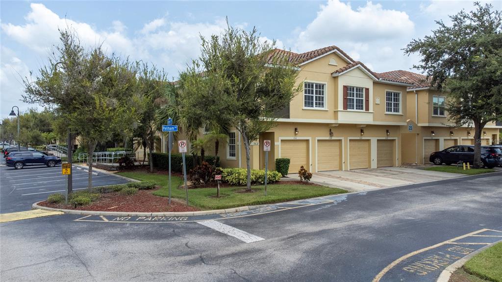 An exterior view of a two-story tan townhouse with multiple garage doors and surrounding landscaping — 7531 PELLHAM WAY UNIT 77, KISSIMMEE, FL