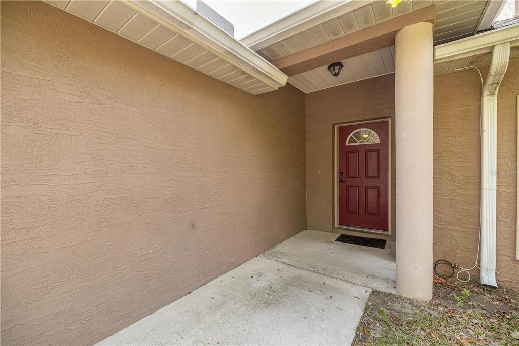 A covered concrete entryway leads to a red front door with a half-moon window — 2635 NE 7TH STREET UNIT 102, OCALA, FL
