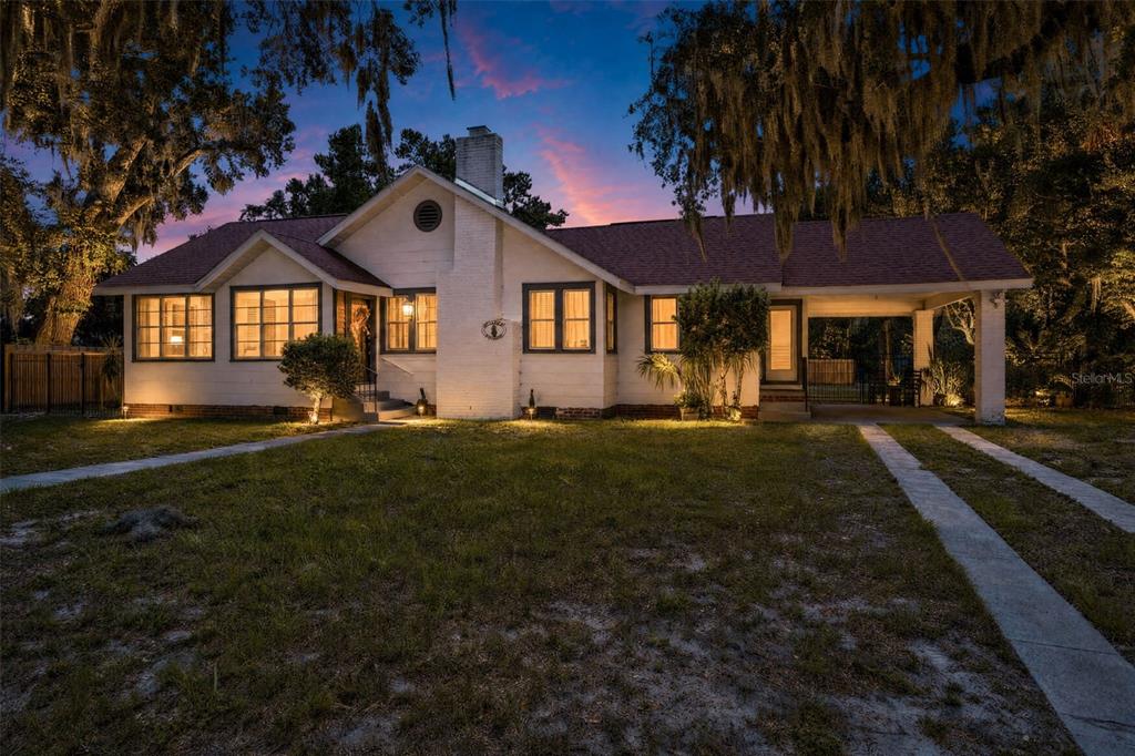 A white single-story house with a brick chimney and attached carport at dusk — 5845 GRAND BOULEVARD, NEW PORT RICHEY, FL