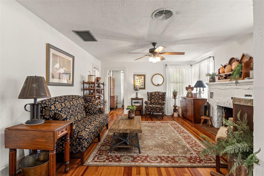 A living room features hardwood floors, a patterned sofa, a fireplace, and a ceiling fan — 5845 GRAND BOULEVARD, NEW PORT RICHEY, FL