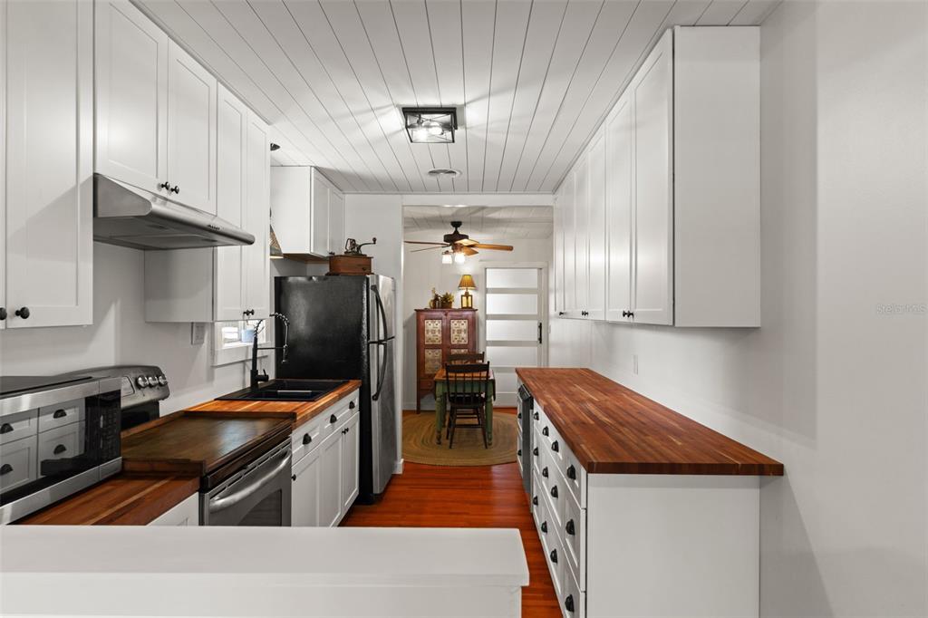 A galley kitchen features white cabinets, butcher block countertops, and a wood-plank ceiling — 5845 GRAND BOULEVARD, NEW PORT RICHEY, FL