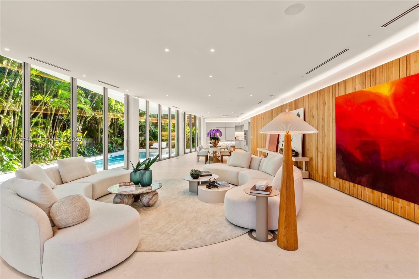 A modern living room features a curved sofa, wood-paneled wall, large abstract art, and floor-to-ceiling windows — 1616 Onaway Dr, Miami FL 33133, MIAMI, FL