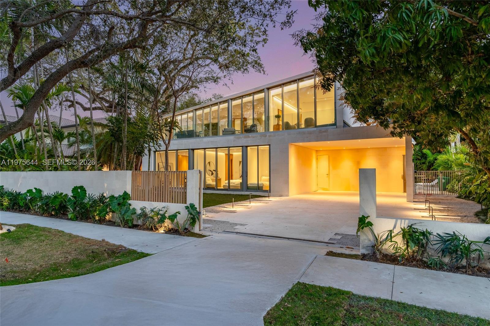 A modern two-story concrete house with floor-to-ceiling glass windows and a covered carport at dusk — 1616 Onaway Dr, Miami FL 33133, MIAMI, FL
