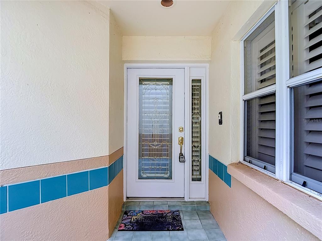 A white front door with a decorative glass insert sits on a tiled porch — 15886 SANCTUARY DRIVE, TAMPA, FL