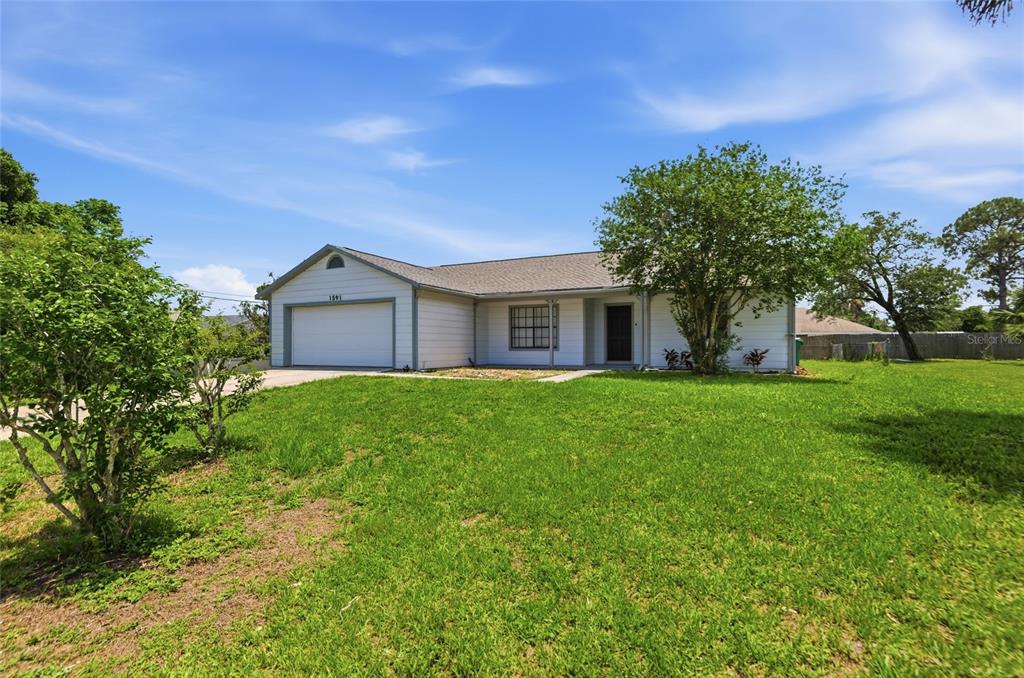 A single-story house with light siding, a front-facing garage, and a large grassy yard — 1591 MALALUKA STREET, DELTONA, FL