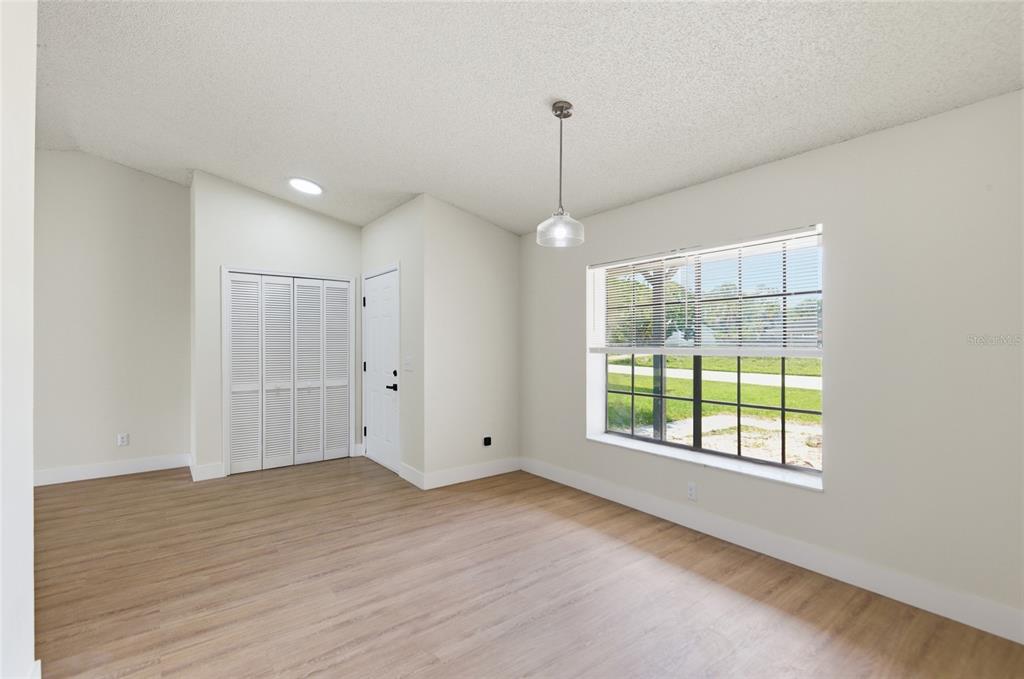 A bright room with light wood-look flooring, a single pendant light, and a large window — 1591 MALALUKA STREET, DELTONA, FL