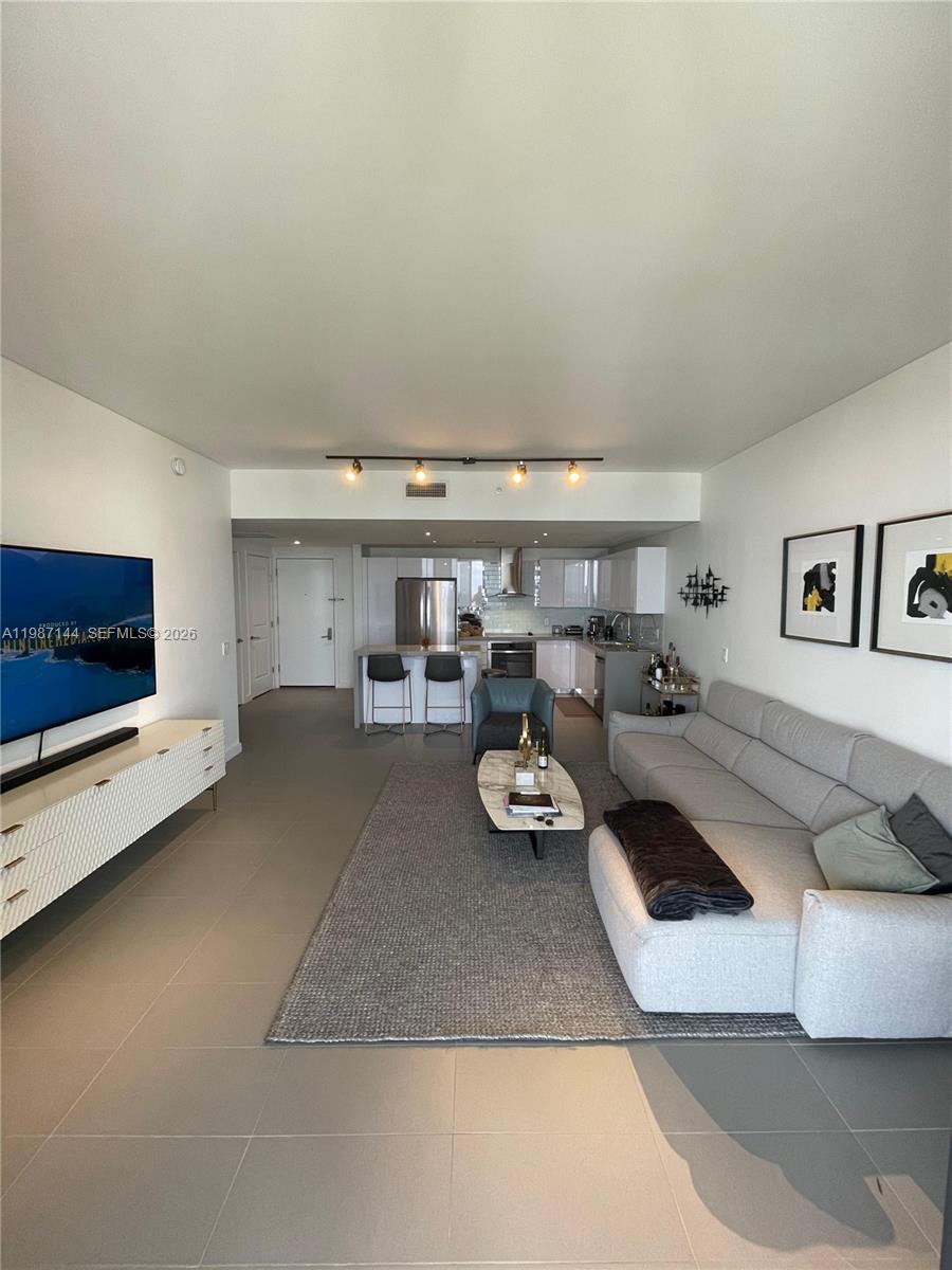 A modern living room features a grey sectional sofa, a white media console, and an open kitchen — 1600 NE 1st Ave # 3717, Miami FL 33132, MIAMI, FL
