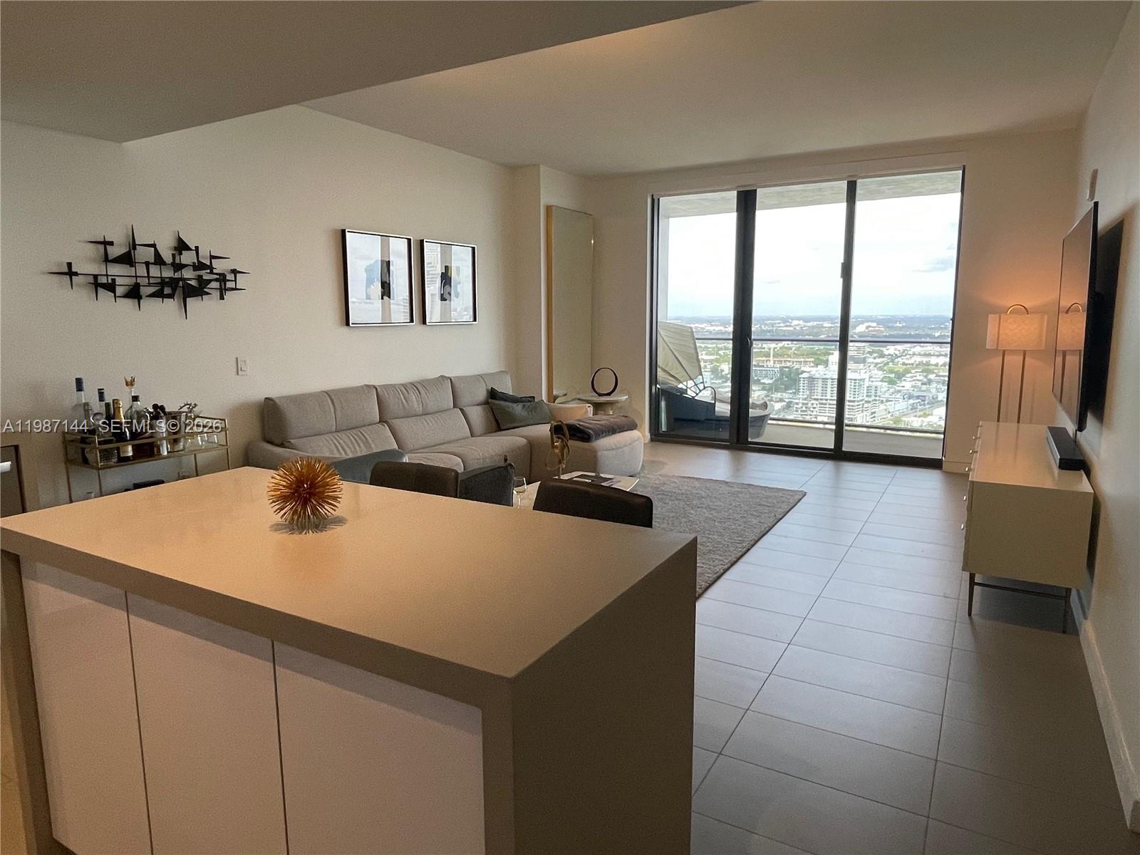A modern living room features a grey sectional sofa, tile flooring, and floor-to-ceiling windows — 1600 NE 1st Ave # 3717, Miami FL 33132, MIAMI, FL