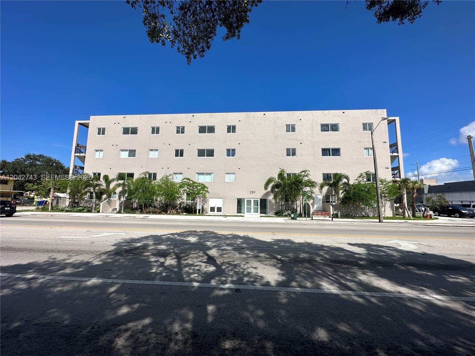 A four-story beige apartment building stands behind a street with trees and parked cars — 2311 NW 22nd Ave, Miami FL 33142, MIAMI, FL