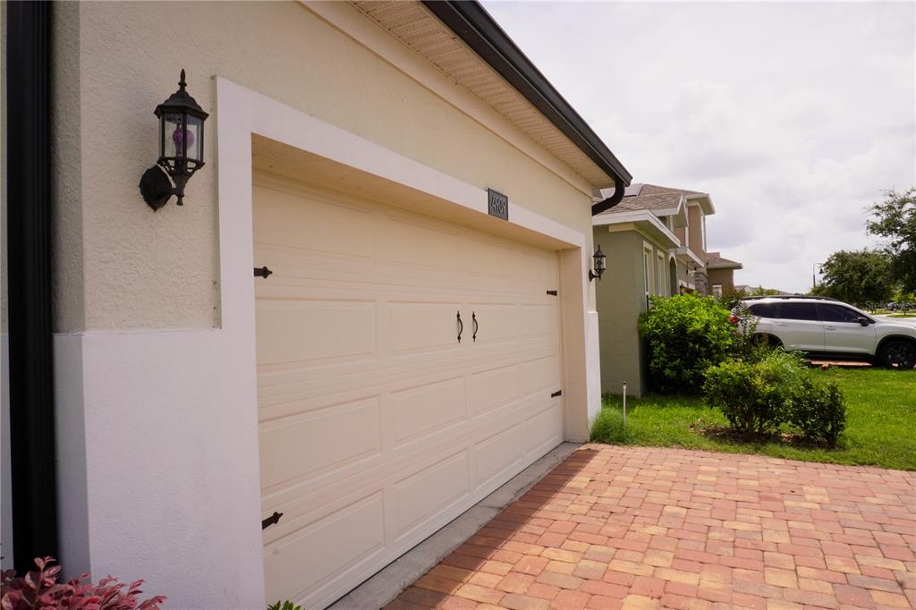 A beige garage door with decorative hardware is set in a stucco exterior with pavers — 4909 OLIVIA COURT, ST CLOUD, FL