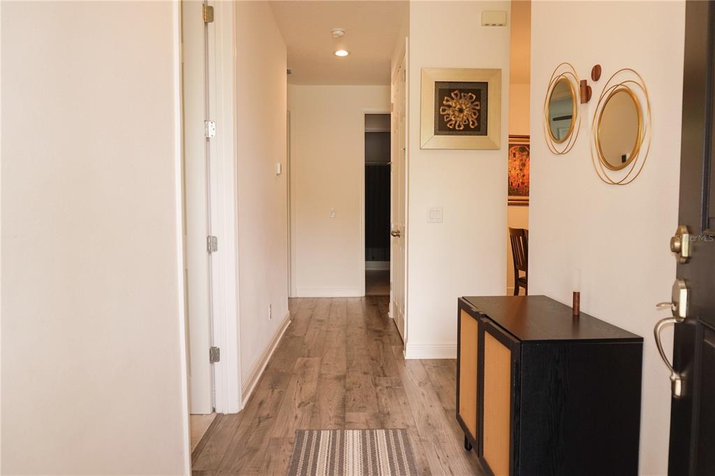 An entryway with wood-look flooring, a dark cabinet, wall mirrors, and a hallway leading inside — 4909 OLIVIA COURT, ST CLOUD, FL
