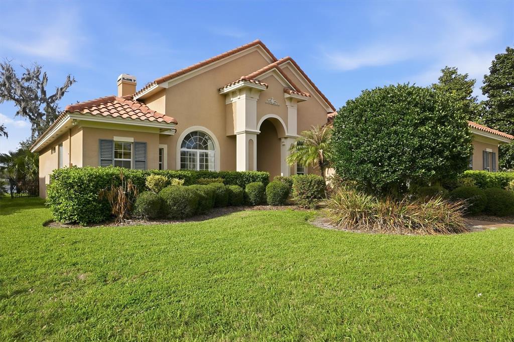 A tan stucco house with a tiled roof and arched entryway sits behind manicured hedges — 13 NEW OAK LEAF DRIVE, PALM COAST, FL