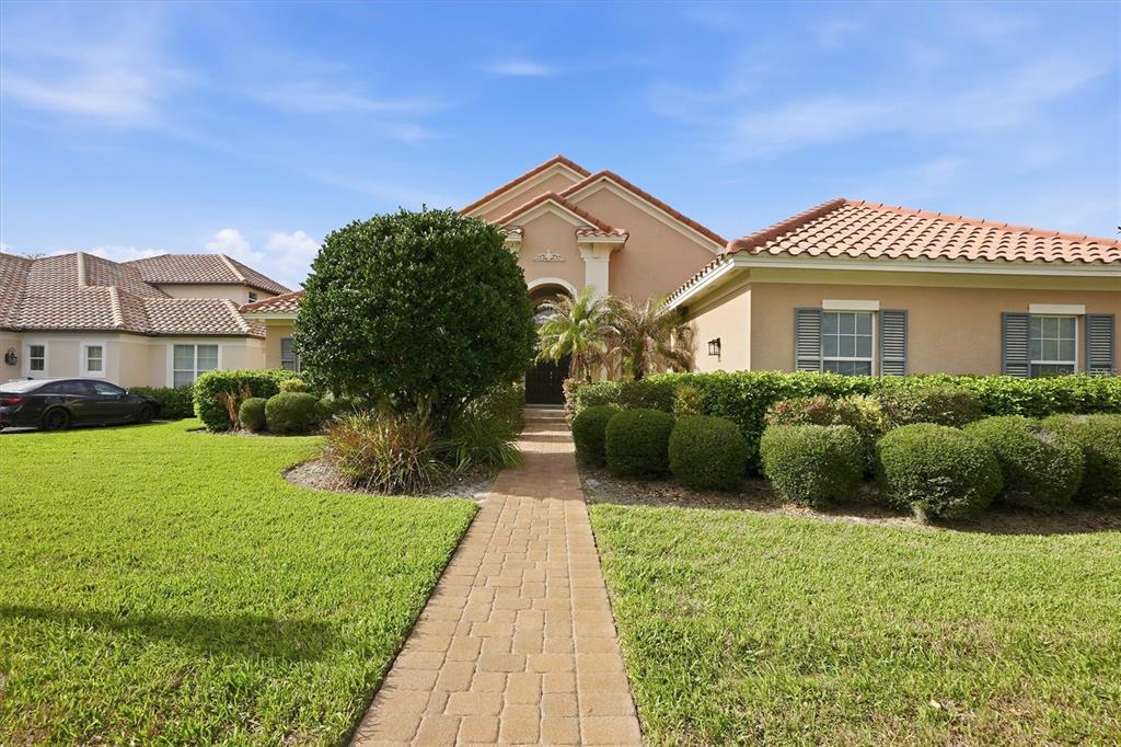 A tan house with a tiled roof and a brick walkway leading to the entrance — 13 NEW OAK LEAF DRIVE, PALM COAST, FL