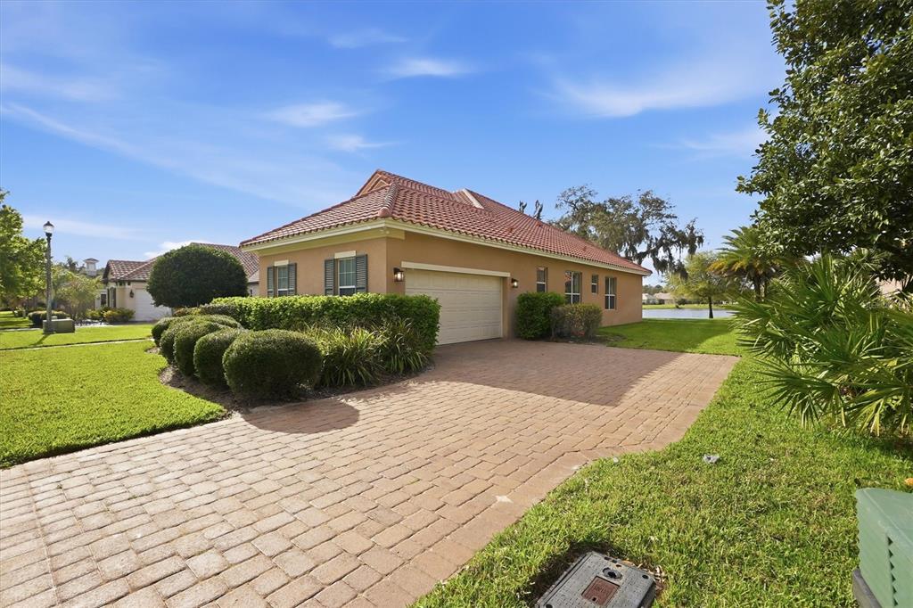 A tan house with a red tile roof and a brick driveway sits on a lawn — 13 NEW OAK LEAF DRIVE, PALM COAST, FL