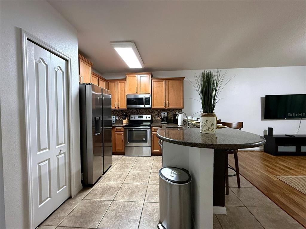 A kitchen features wood cabinets, stainless steel appliances, a granite island, and tiled flooring — 1056 CYPRESS POINTE BOULEVARD, DAVENPORT, FL
