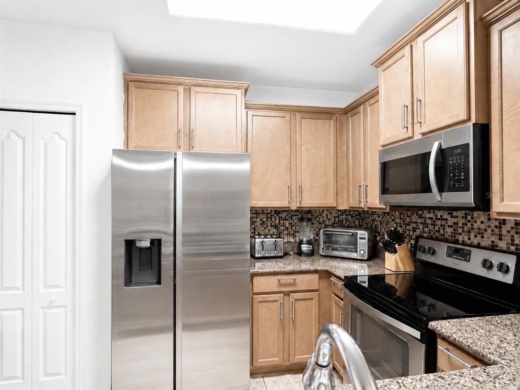 A kitchen features light wood cabinets, stainless steel appliances, and a mosaic tile backsplash — 1056 CYPRESS POINTE BOULEVARD, DAVENPORT, FL