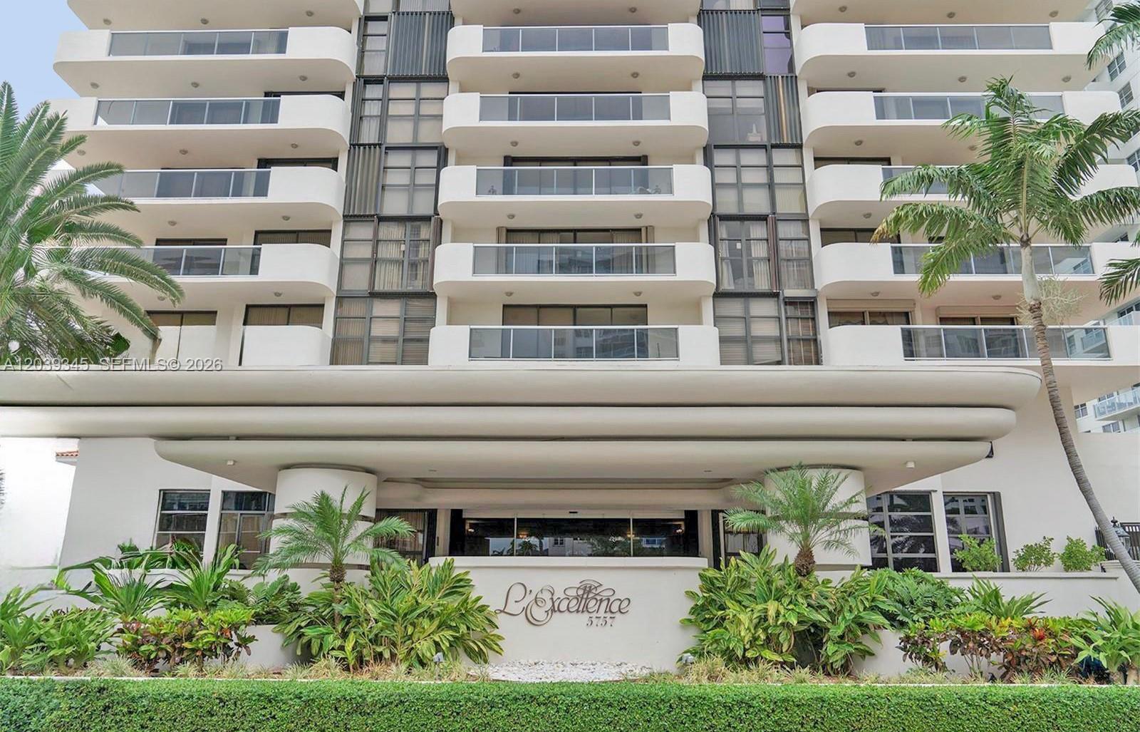 The exterior of a multi-story residential building features balconies and a landscaped entrance area — 5757 Collins Ave # 702, Miami Beach FL 33140, MIAMI BEACH, FL
