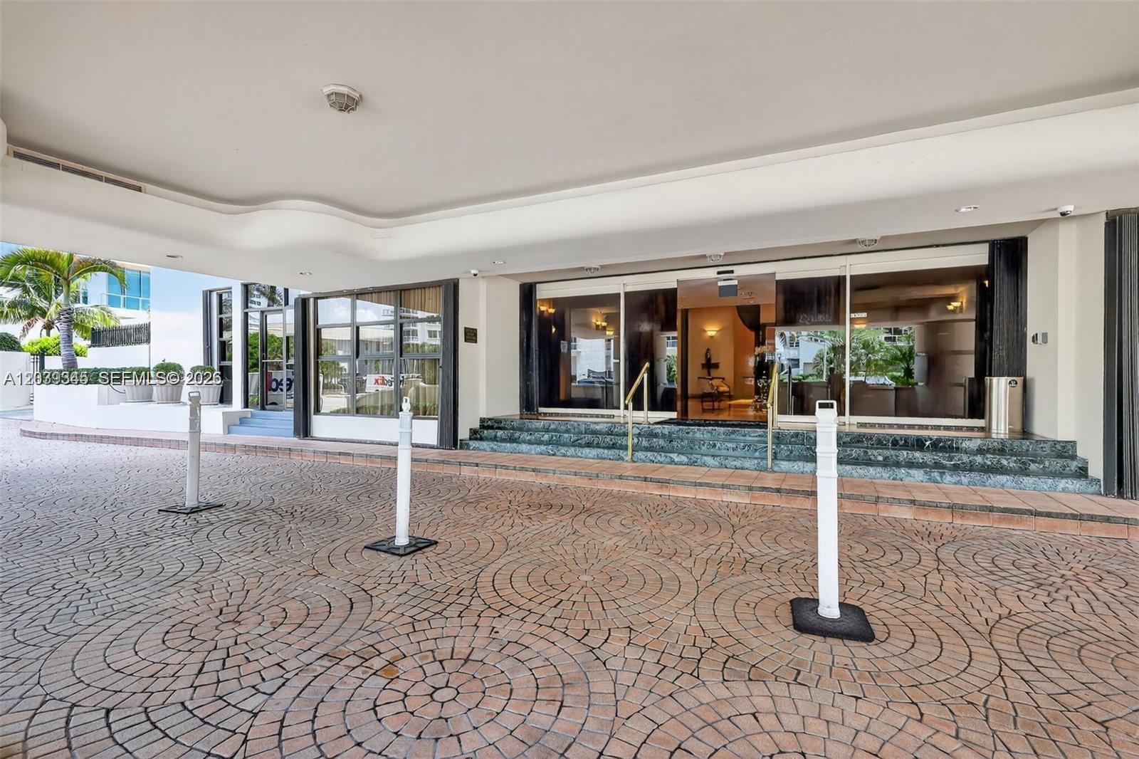 The exterior entrance of a building features a paved circular driveway and glass doors — 5757 Collins Ave # 702, Miami Beach FL 33140, MIAMI BEACH, FL