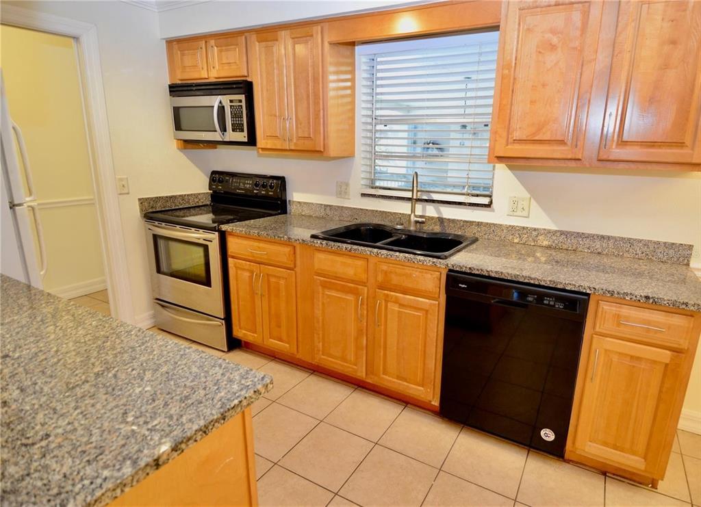 A two-story building features a screened-in balcony, a palm tree, and a white privacy wall — 3360 S OSPREY AVENUE UNIT 201B, SARASOTA, FL