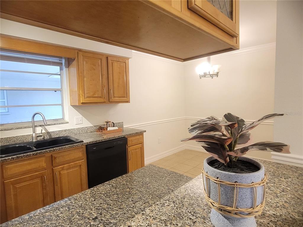 A kitchen features wood cabinets, granite countertops, a black dishwasher, and a dining area — 3360 S OSPREY AVENUE UNIT 201B, SARASOTA, FL