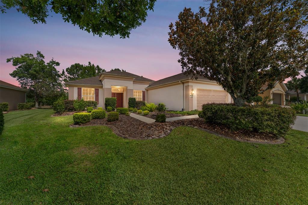 A single-story suburban house with a tan stucco exterior, a two-car garage, and landscaped lawn — 12947 SE 97TH TERRACE ROAD, SUMMERFIELD, FL