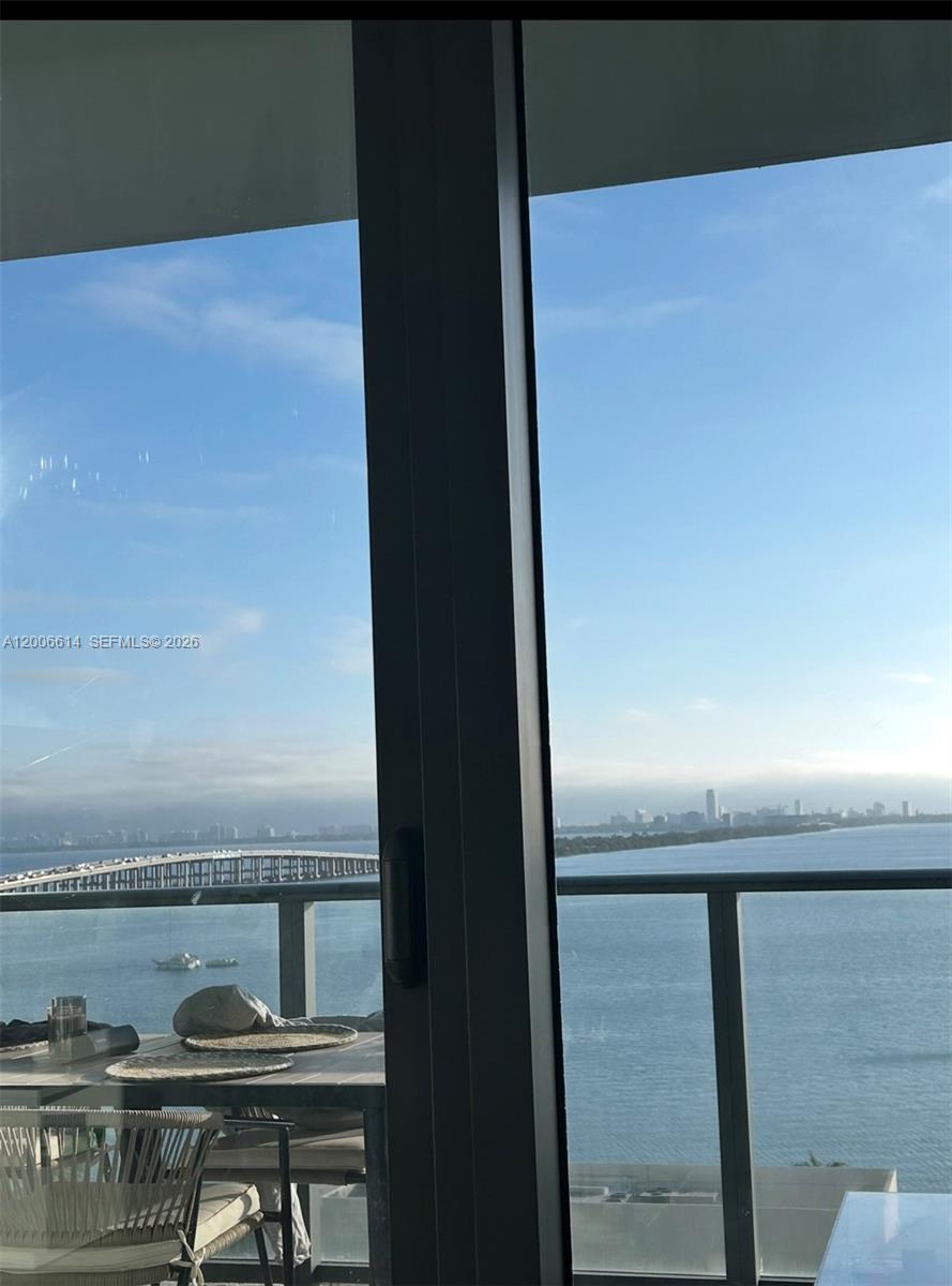 A balcony with a table and chairs overlooks a bay, a bridge, and a city skyline — 480 NE 31st St # 905, Miami FL 33137, MIAMI, FL