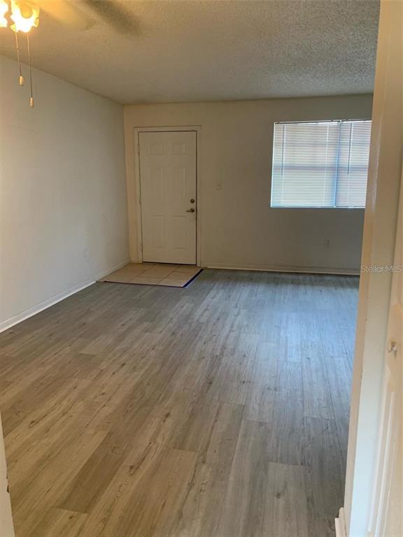 An empty living room features light wood-look flooring, a white front door, and a window — 12403 HIBISCUS OAK PLACE UNIT 202, TAMPA, FL