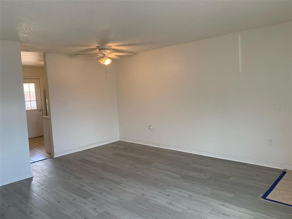 An empty room features light gray wood-look flooring, white walls, and a ceiling fan — 12403 HIBISCUS OAK PLACE UNIT 202, TAMPA, FL