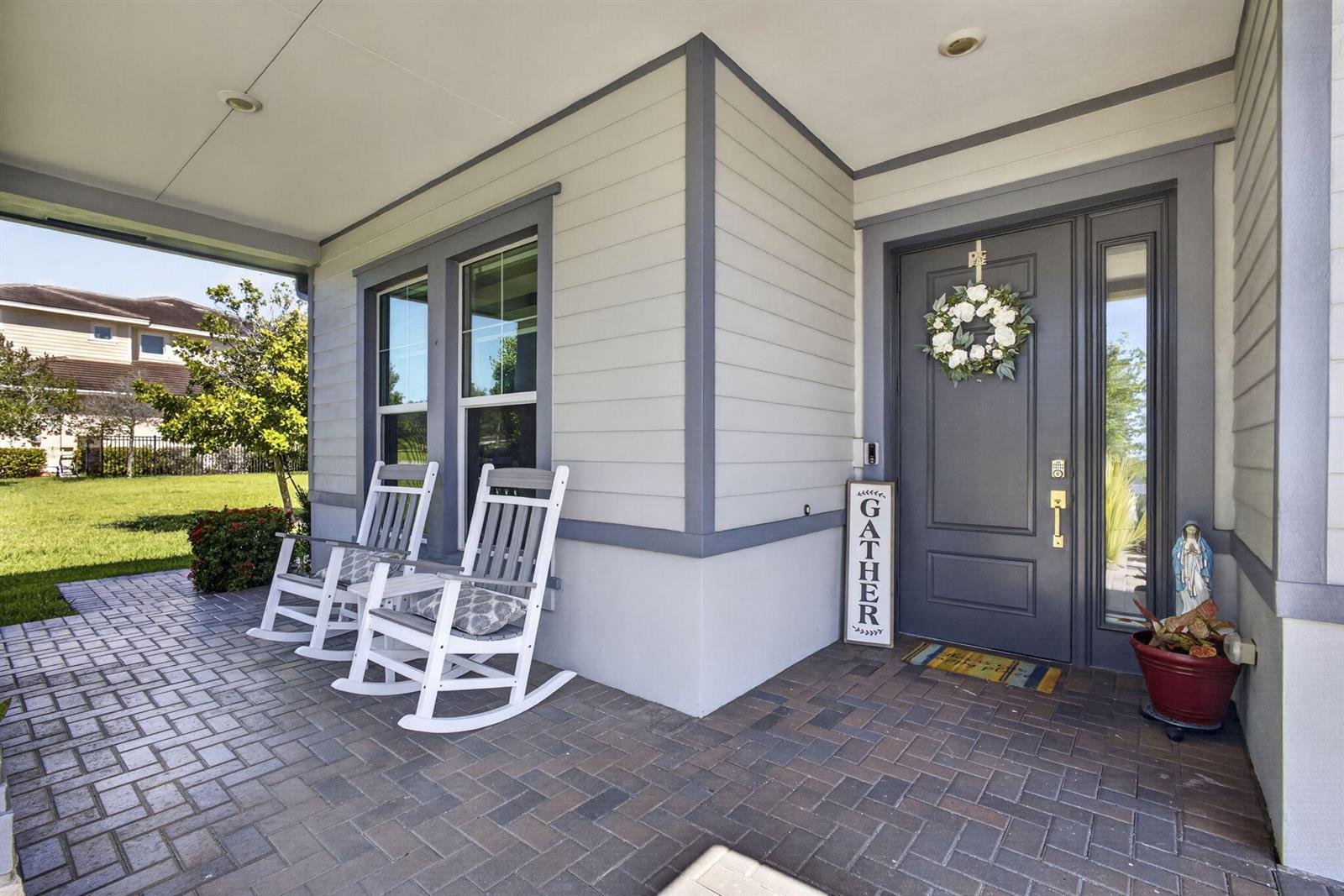A covered porch features two rocking chairs, a dark front door, and brick pavers — 19599 Split Rail Run, Loxahatchee FL 33470, LOXAHATCHEE, FL