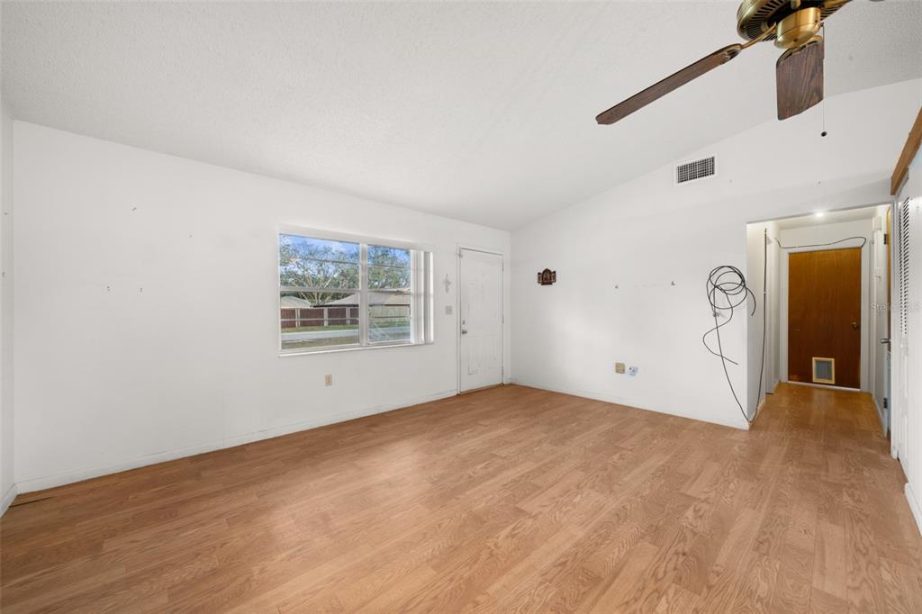 An empty living room with light wood-look flooring, white walls, a ceiling fan, and windows — 2067 N TERRAPIN ROAD, AVON PARK, FL